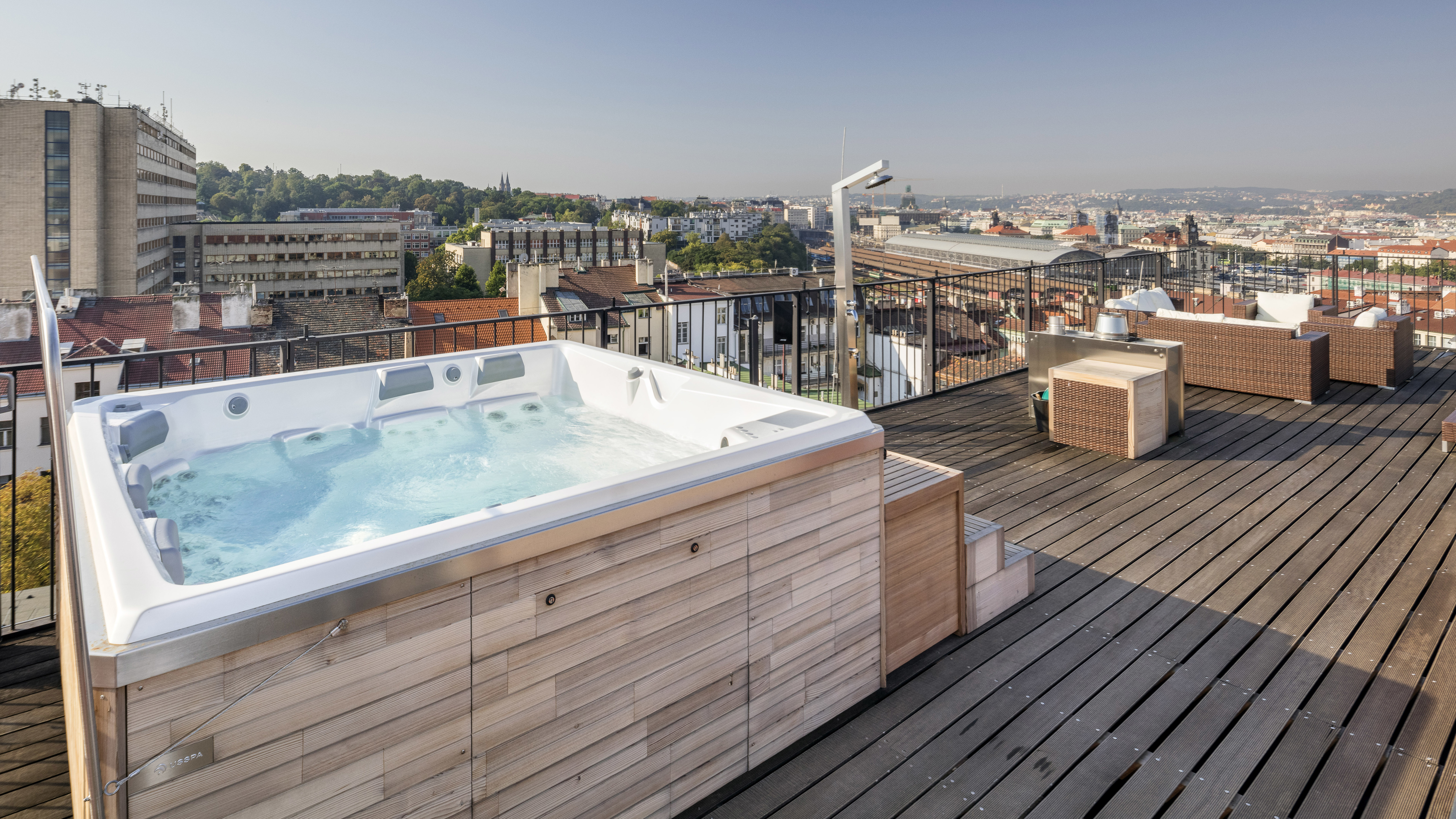 Premium-USSPA Whirlpool auf einer Holzterrasse mit Aussicht über eine Stadt mit historischen und modernen Gebäuden.