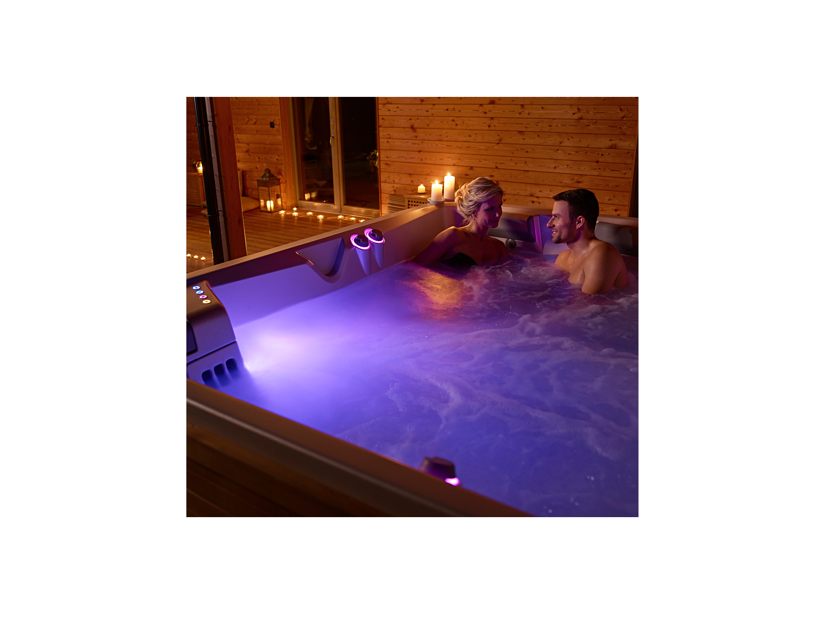 Ein Paar genießt die entspannende Atmosphäre in einem hochwertigen USSPA Whirlpool von ActiveSpa, beleuchtet mit sanftem lila Licht und umgeben von Kerzen in einer gemütlichen Holzumgebung.