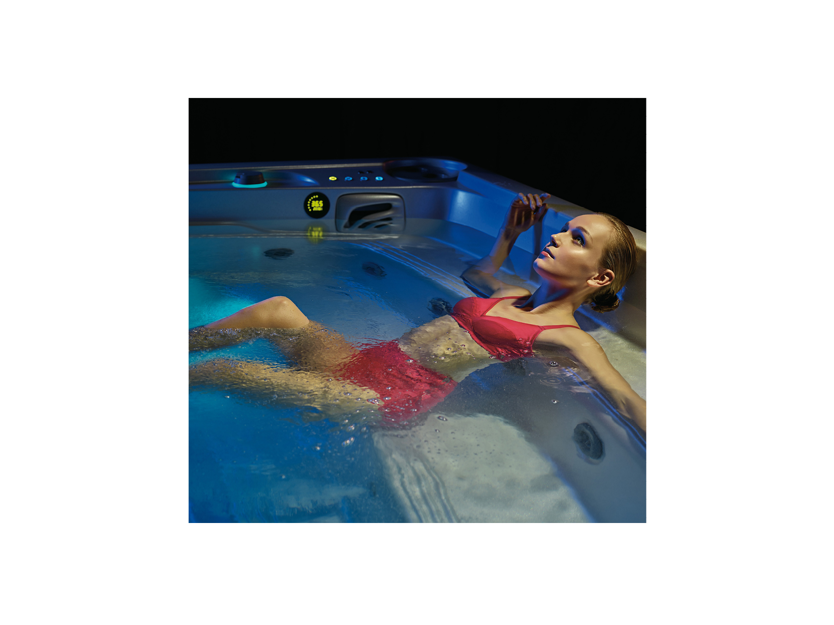 Frau in rotem Bikini entspannt sich in einem hochwertigen USSPA Whirlpool mit blauer Beleuchtung – ideal für private Entspannung und Wellness.